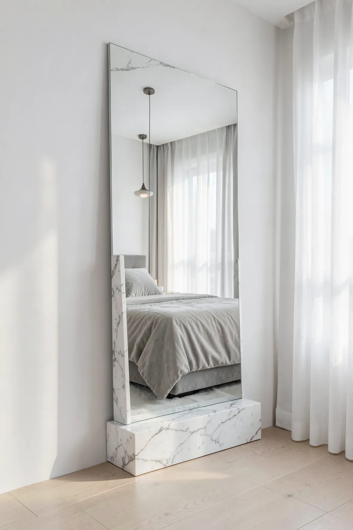 A minimalist floor mirror with a heavy white marble base in a bright, modern bedroom.