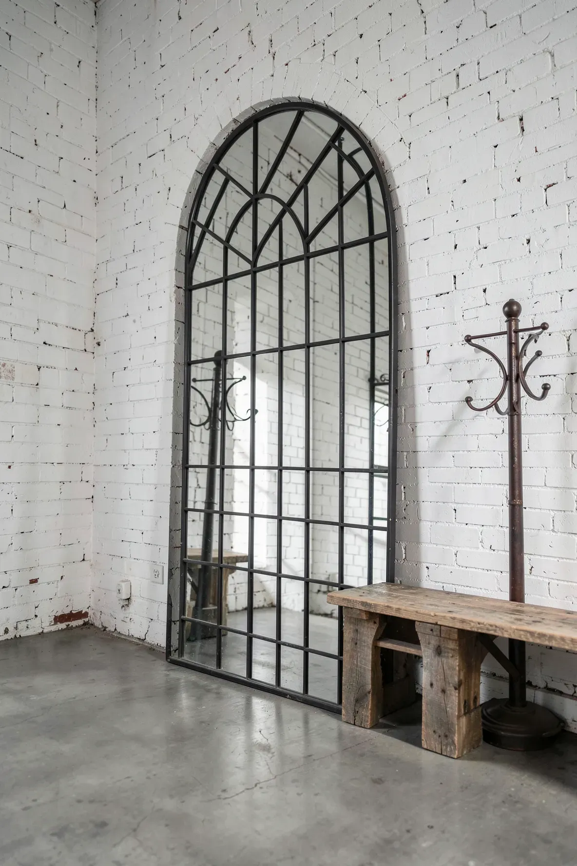 An arched mirror with a black metal grid leaning against a white brick wall in an entryway.