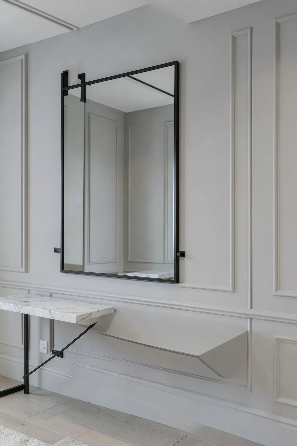 A large black-framed mirror mounted perfectly flat against a grey wall in a modern entryway.