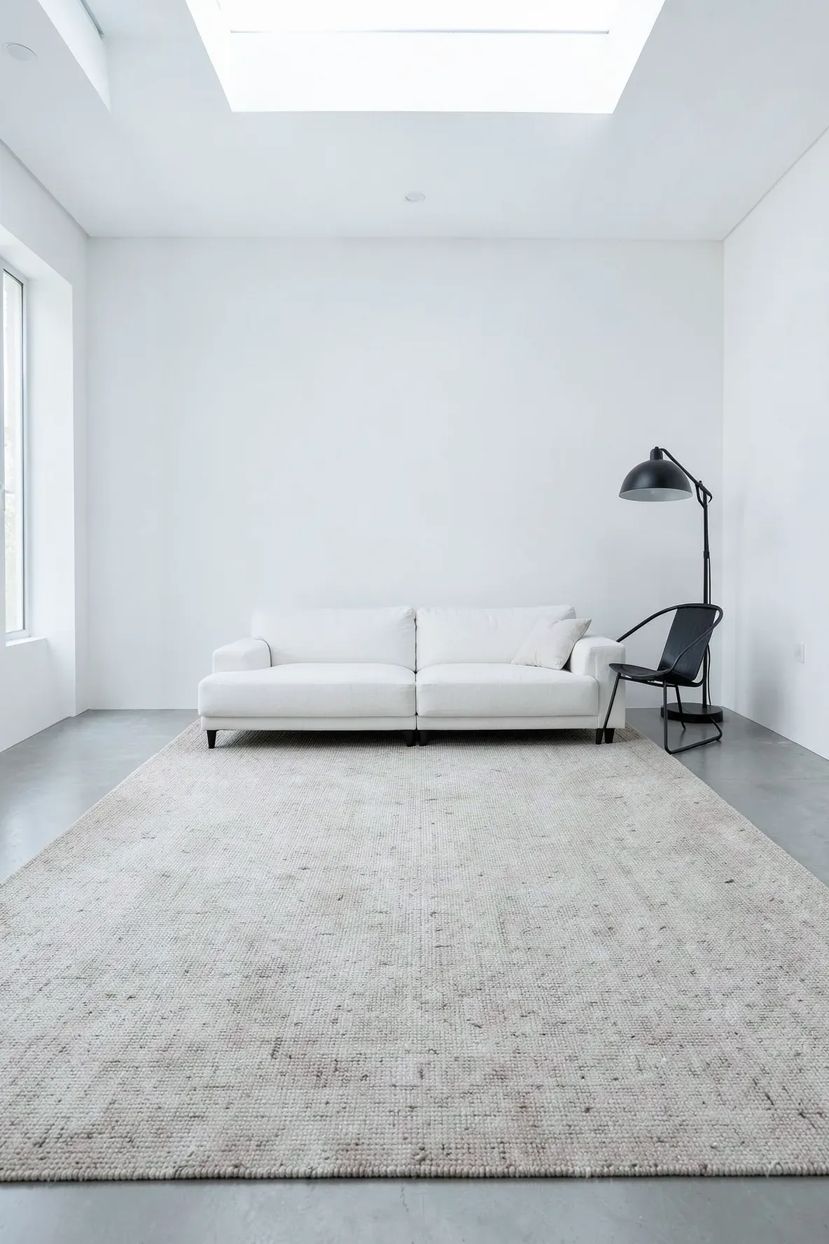 A large flat-weave oatmeal colored rug in a minimalist white living room with modern furniture.
