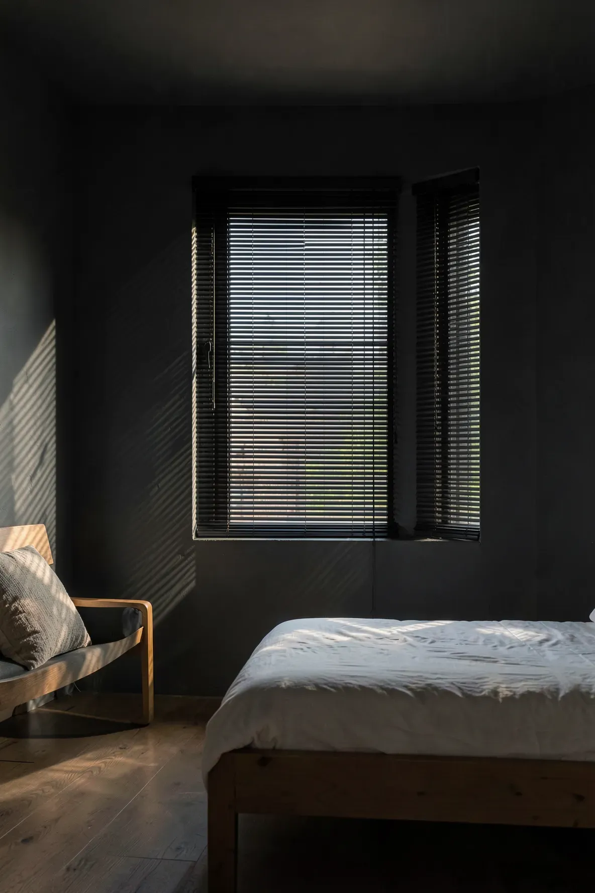 Black bamboo blinds on a bedroom window creating linear shadow patterns on dark walls.