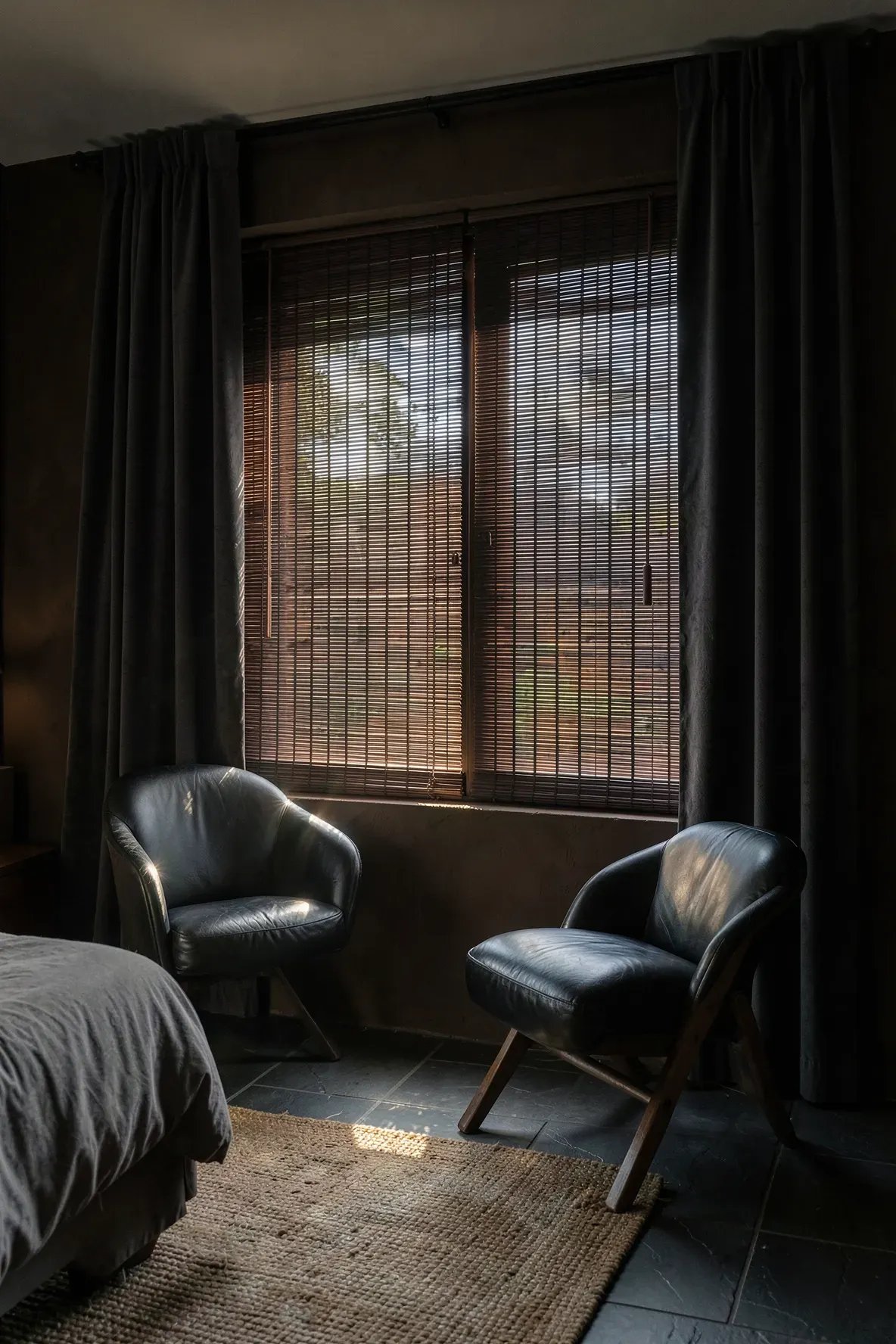 Dark stained bamboo blinds on a window in a moody bedroom with charcoal curtains.
