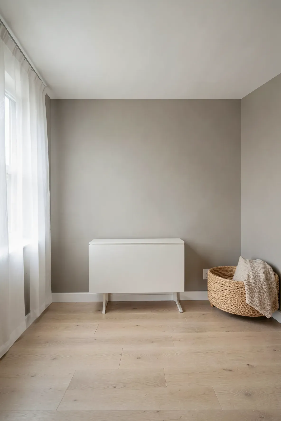 A bright, serene nursery with warm grey walls, light wood floors, and soft natural window lighting.
