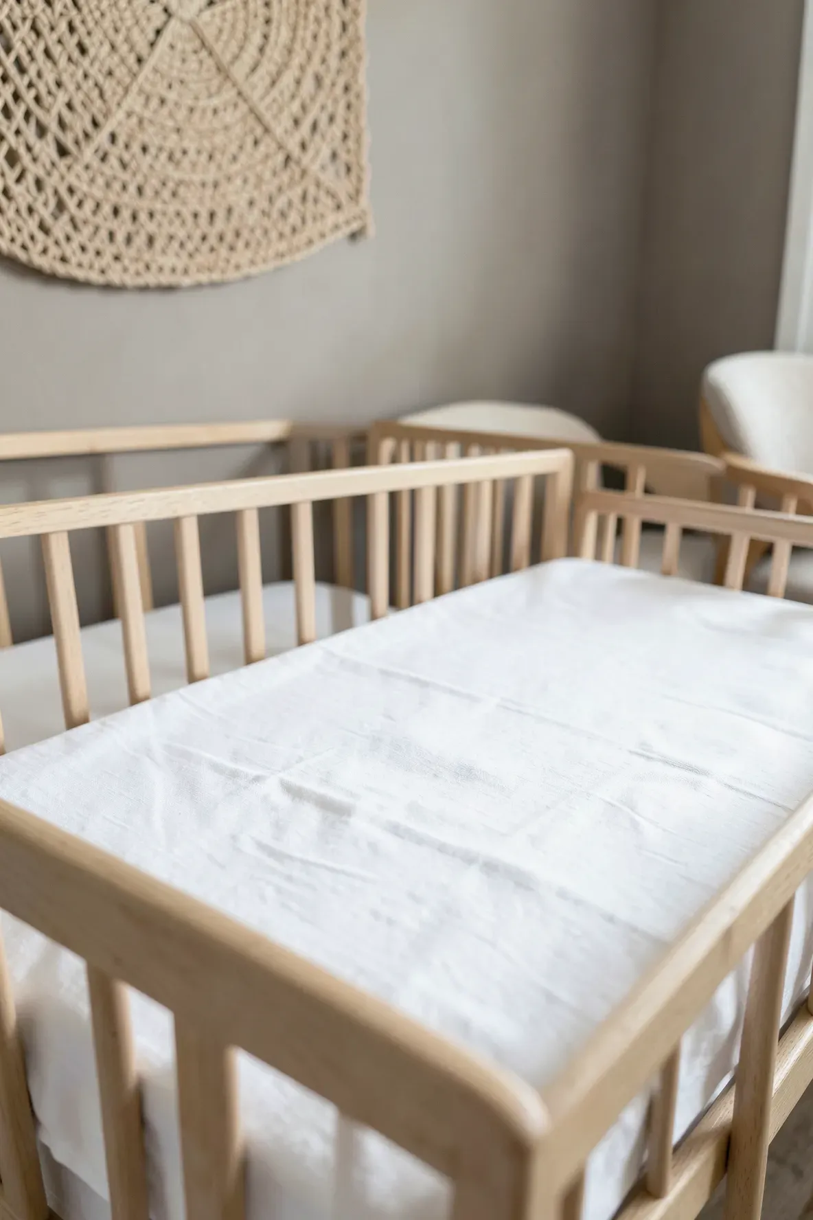 A wooden crib with a neatly fitted white cotton sheet in a bright, minimalist nursery.