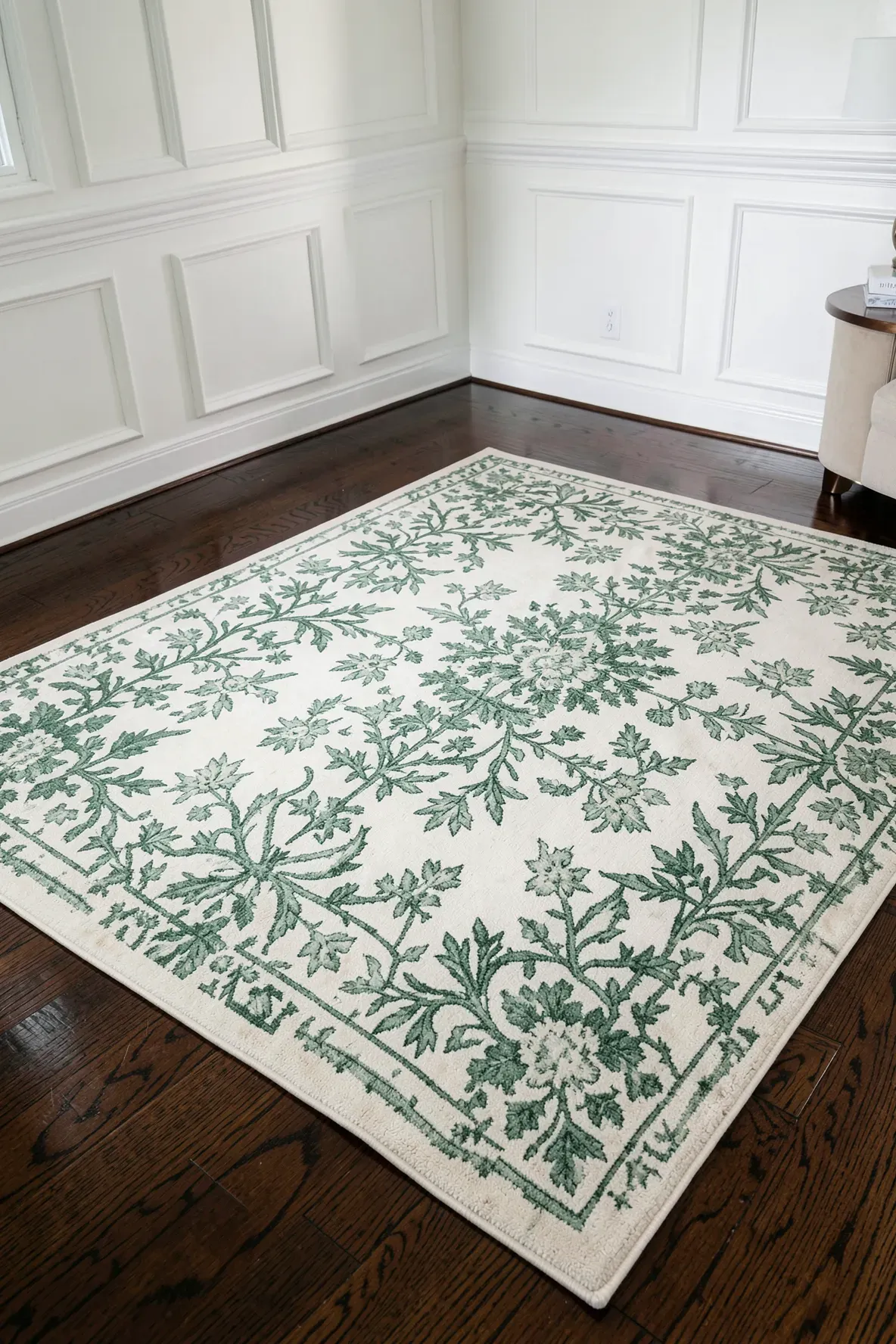 A cream rug with green patterns on dark hardwood floors in a sophisticated living room.
