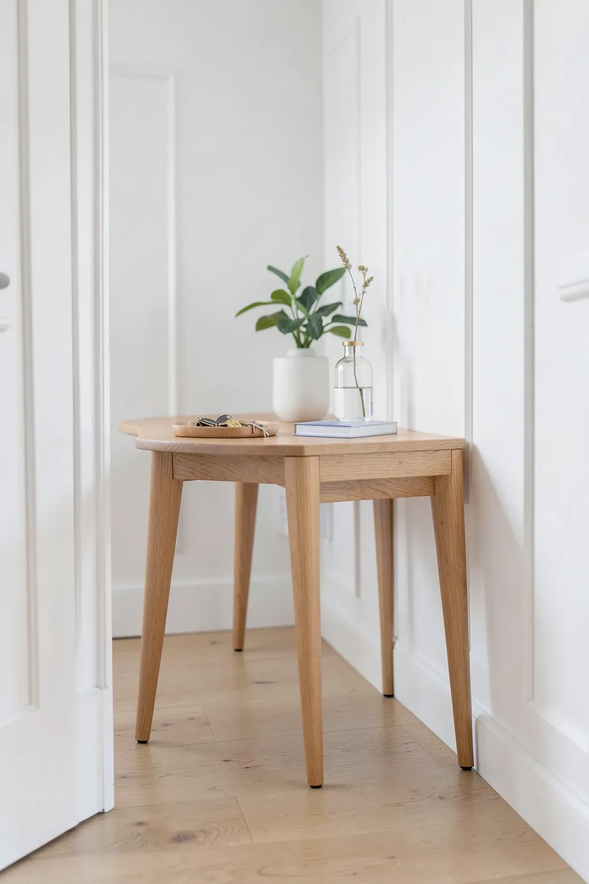 A very thin wooden console table with tapered legs sitting against a wall in a narrow hallway.