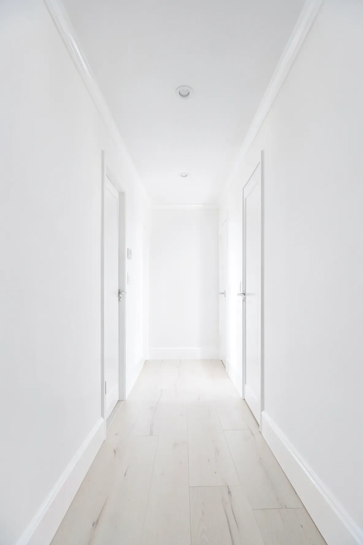 A long narrow hallway painted entirely in bright white from floor to ceiling to make it feel wider.