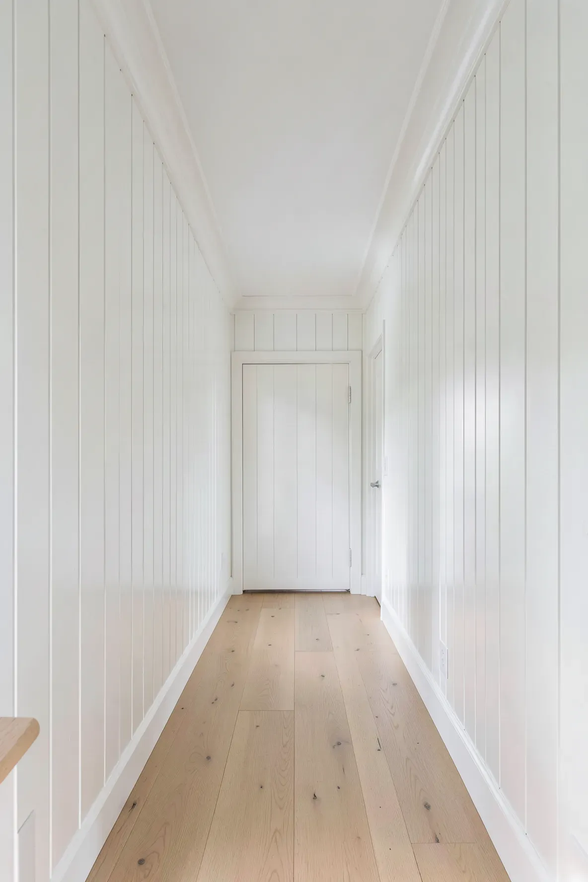 Vertical white shiplap paneling on the walls of a long, narrow, bright hallway.