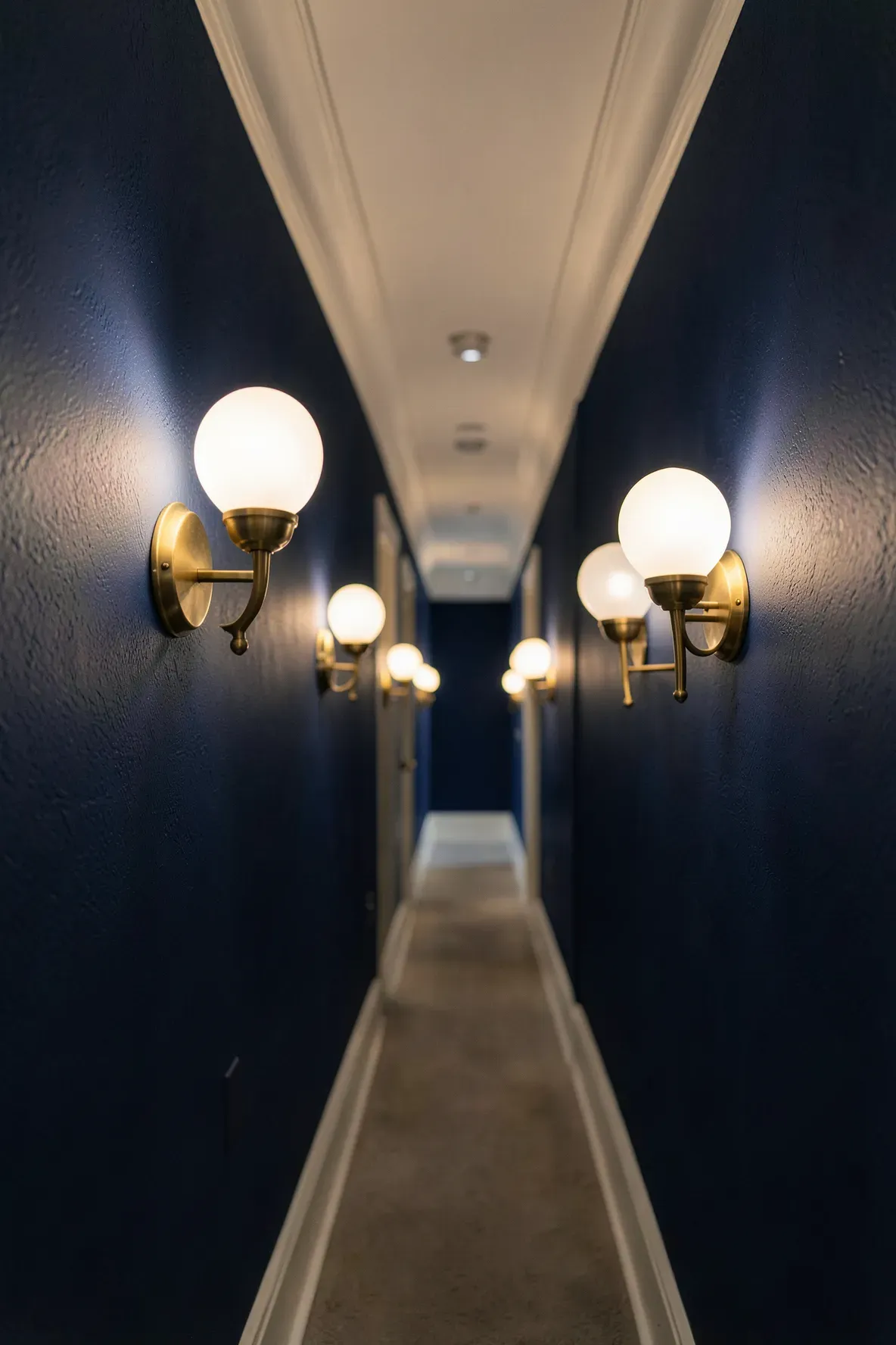 Pairs of symmetrical brass wall sconces lighting up a long narrow hallway.