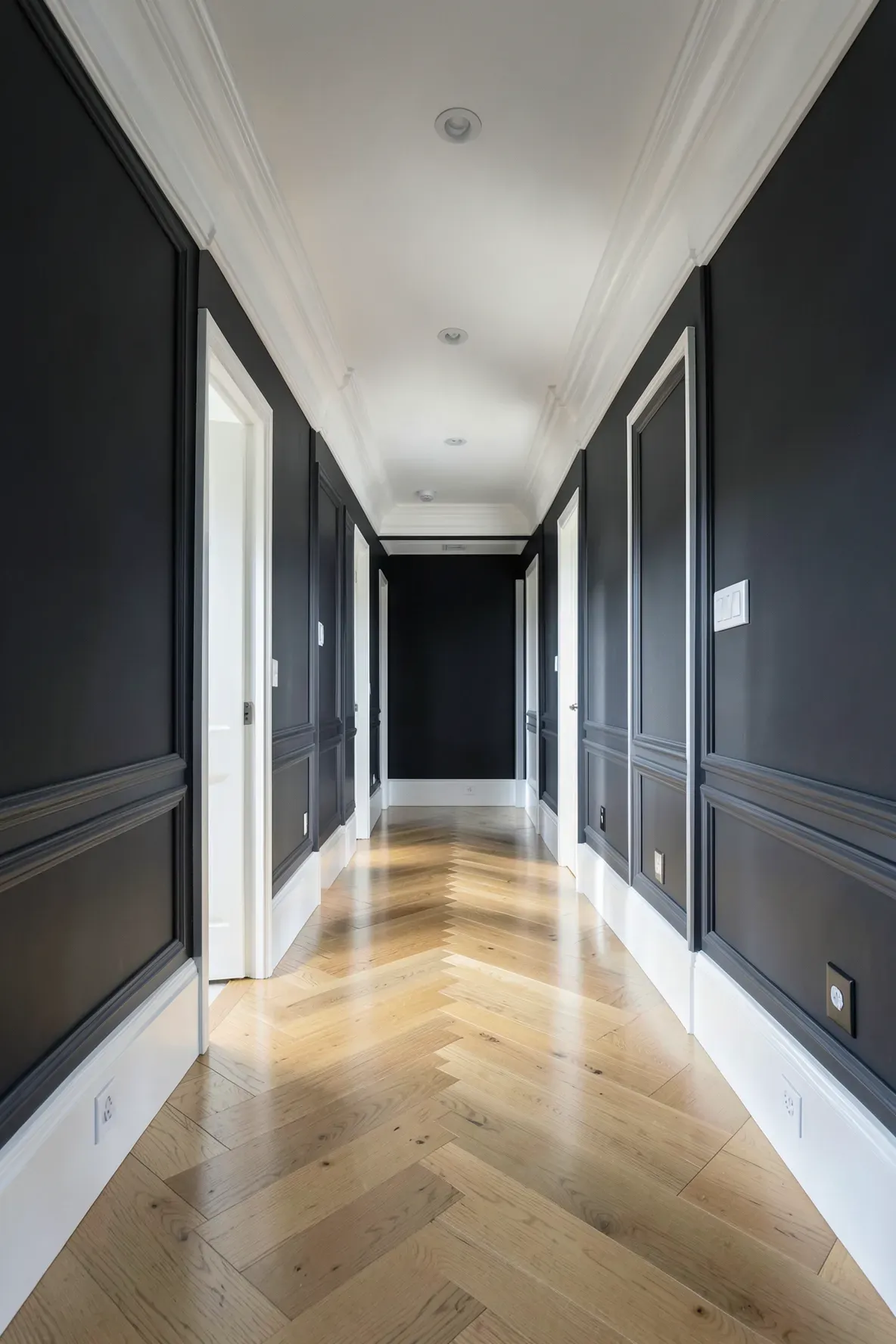 A long narrow hallway with thick white crown molding and baseboards against dark grey walls.