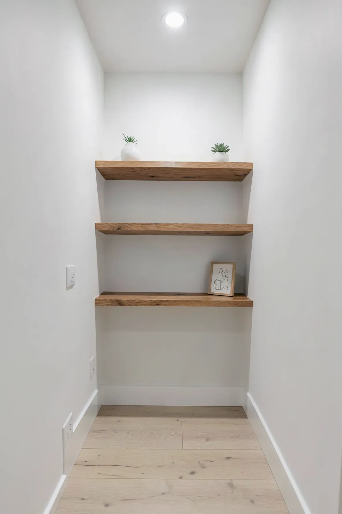 Thin walnut floating shelves with small decor items on a white hallway wall.