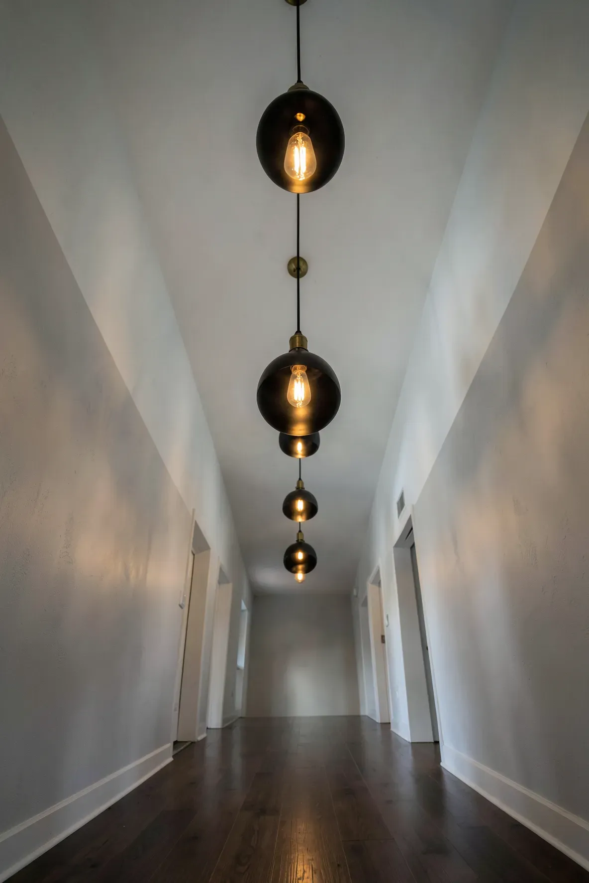 A series of black and brass pendant lights hanging down a long, high-ceilinged hallway.