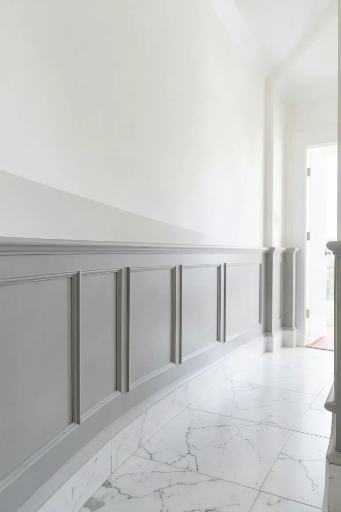 Soft grey half-wall wainscoting with white upper walls in a long narrow hallway.
