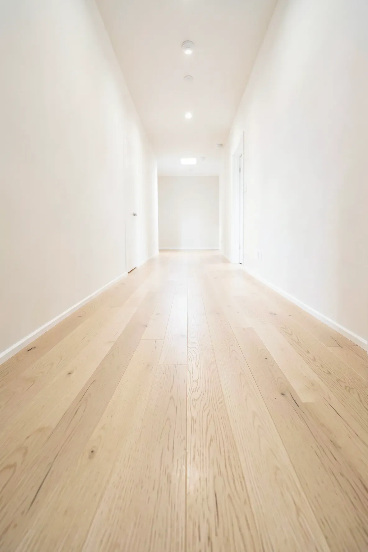 Light maple wood planks laid horizontally in a long hallway to make the space look wider.