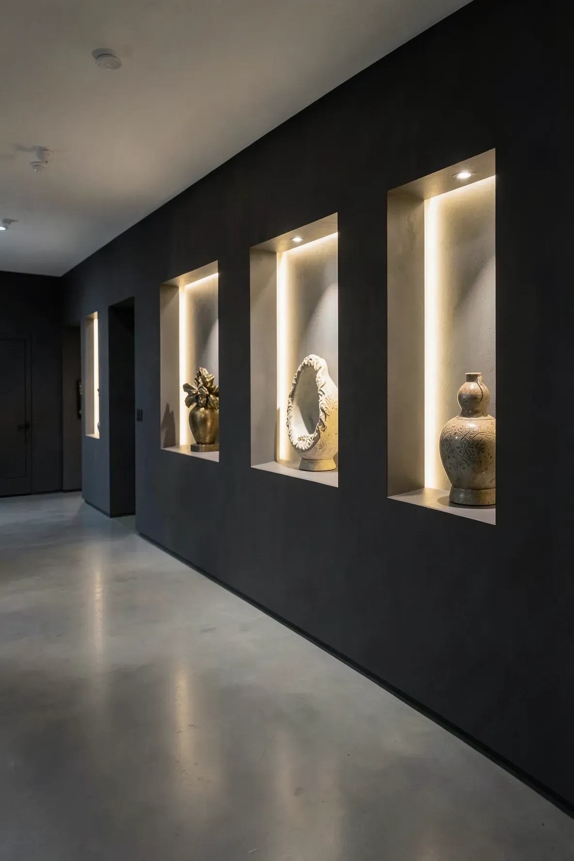 Recessed wall niches with warm LED lighting displaying art in a modern hallway.