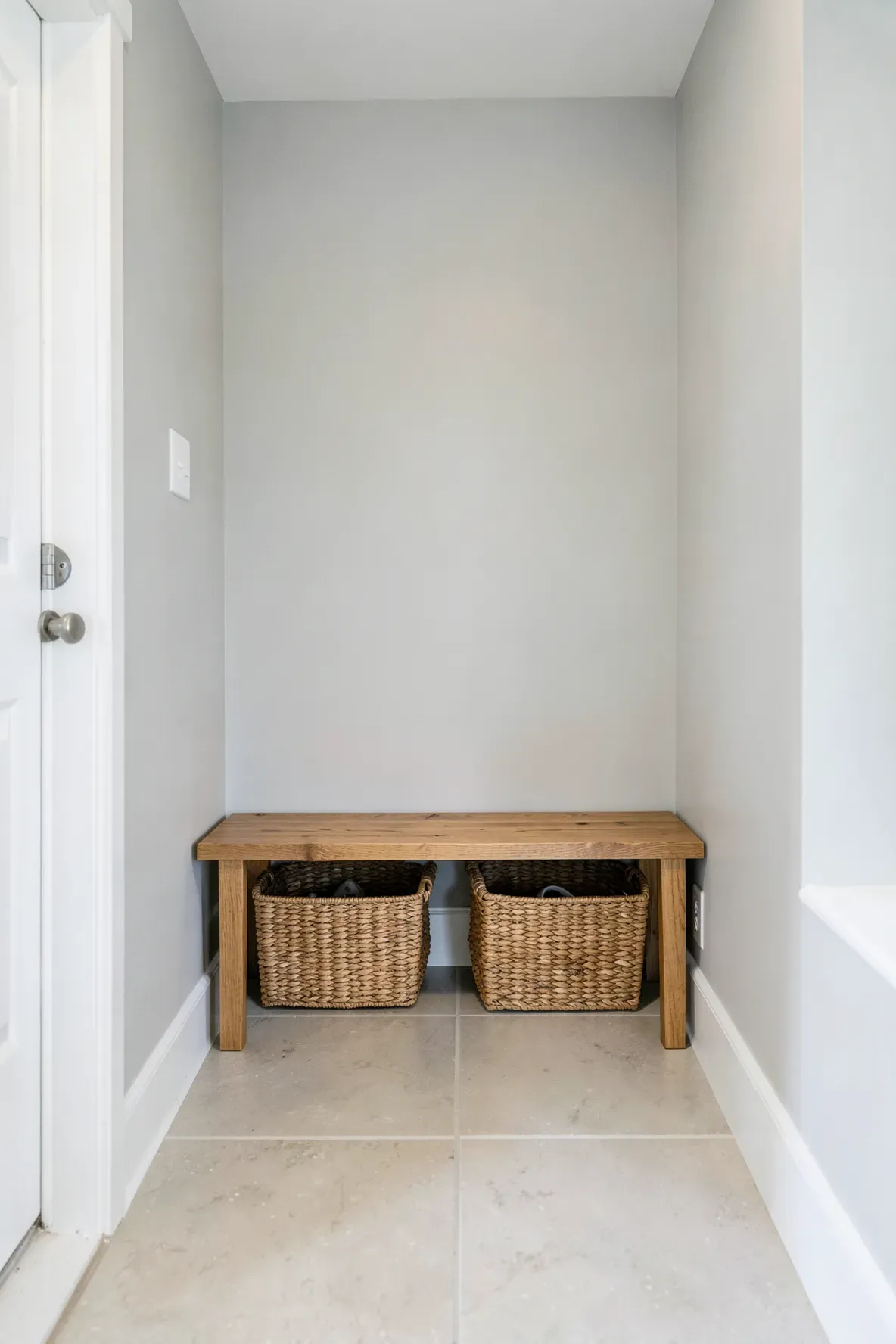 A slim wooden bench with woven baskets underneath in a narrow hallway.