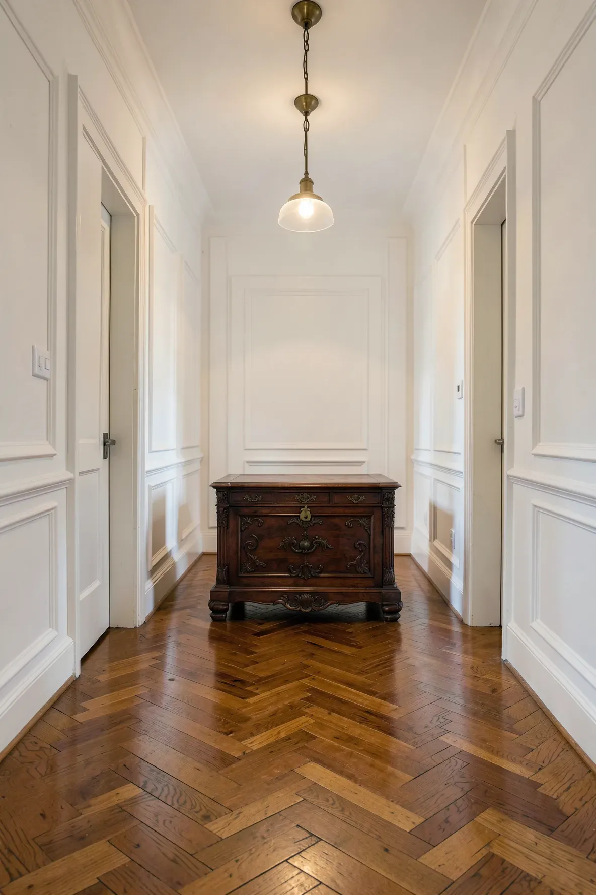 An antique wooden chest at the end of a long narrow hallway with white walls.