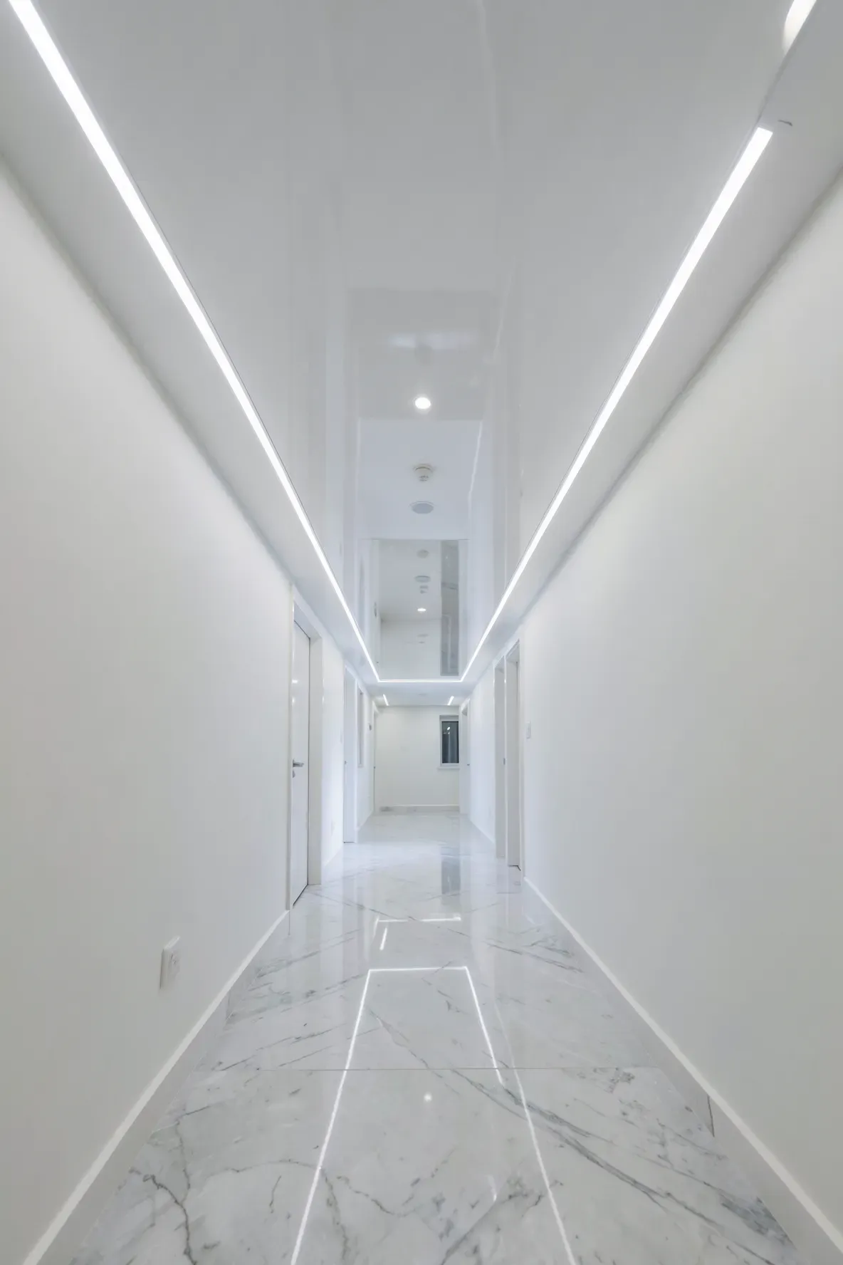 A bright narrow hallway with a high-gloss white ceiling reflecting light to make the space feel wider.