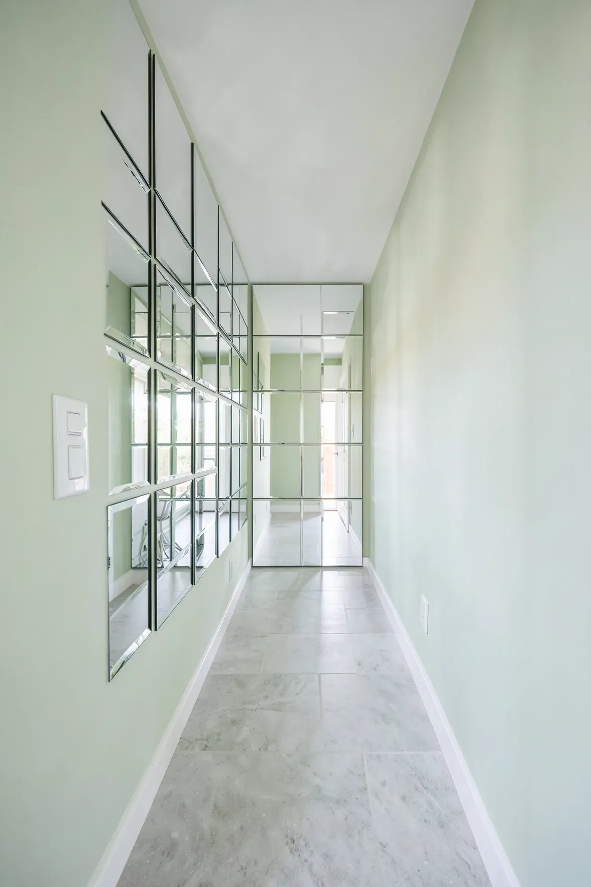 A grid of small square mirrors on a hallway wall reflecting light to make the space feel wider.