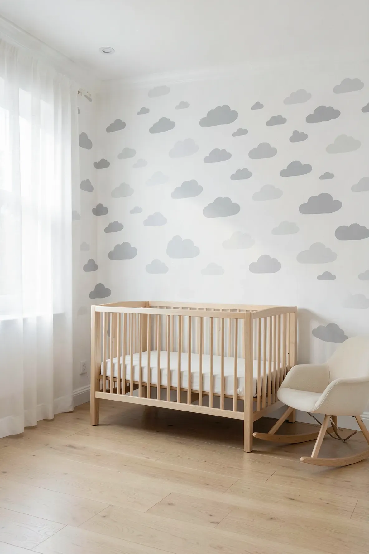 A calm baby nursery with soft grey cloud decals on a white wall behind a wooden crib.