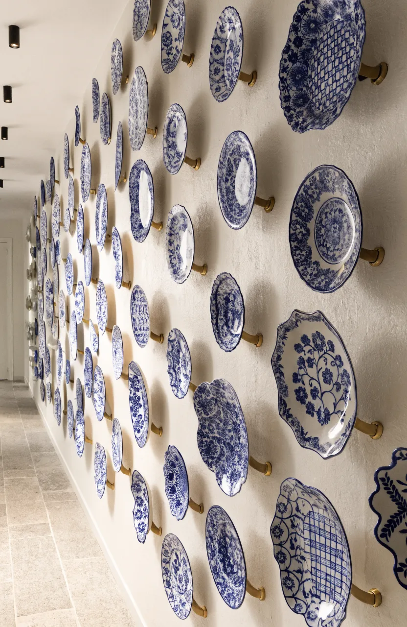 Small blue and white hand-painted ceramic plates displayed on brass brackets along a white hallway wall.