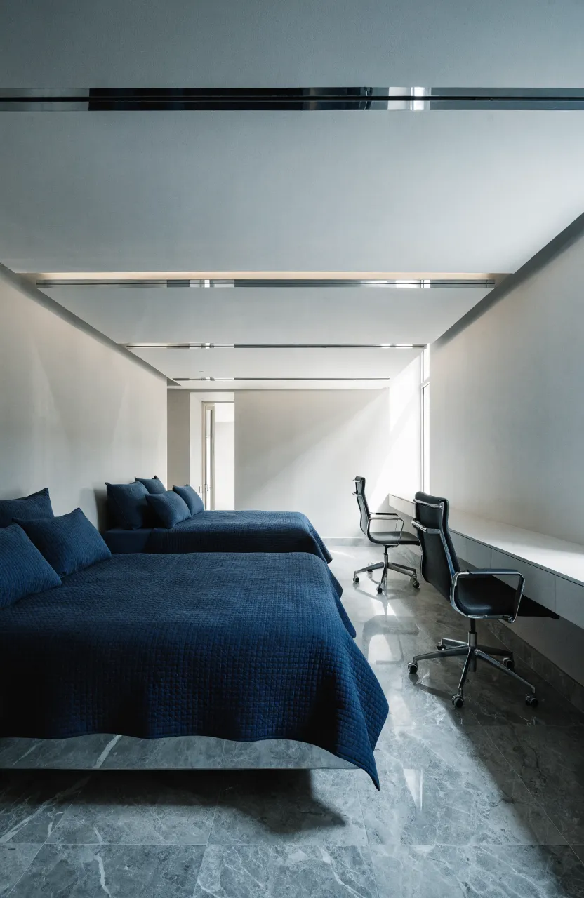 A narrow bedroom featuring two parallel beds and a long, continuous desk along the opposite wall.