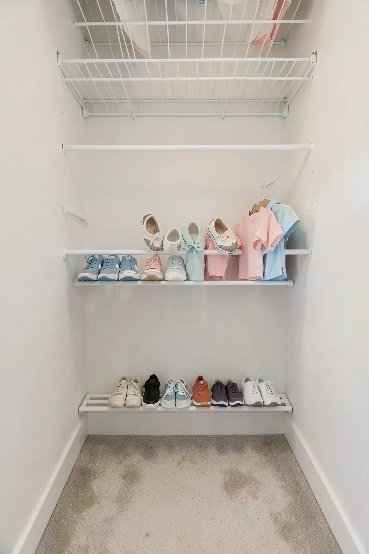 A closet floor organized with two tension rods holding several pairs of kids shoes at an angle.