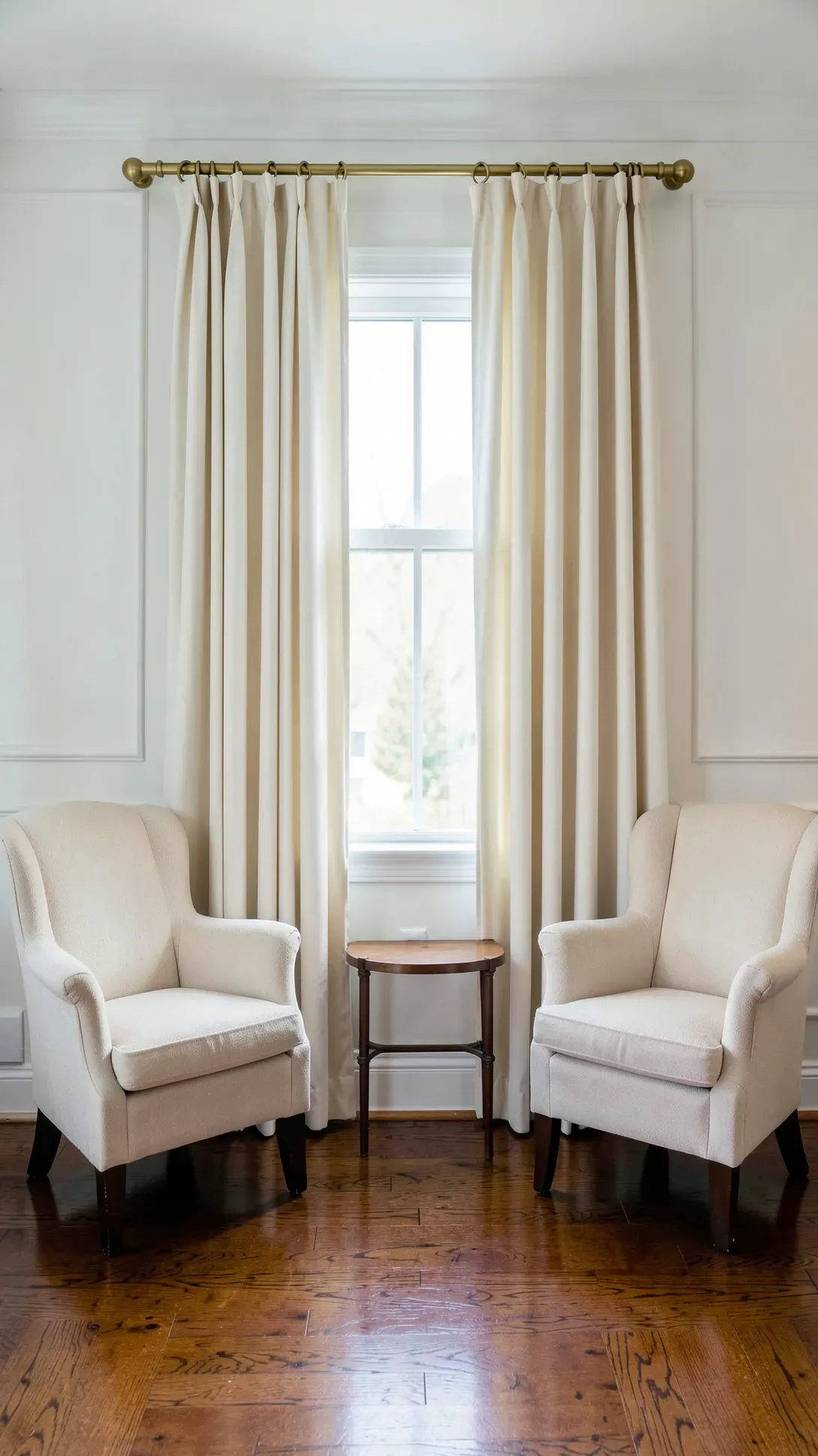 Elegant pinch pleat cotton curtains on a brass rod in a refined living room with wainscoting.