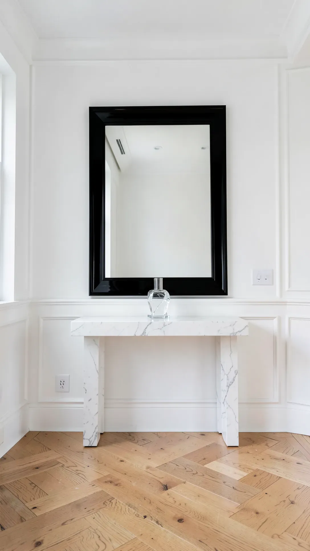 A bold black lacquer mirror hanging above a marble console in a bright white modern foyer.