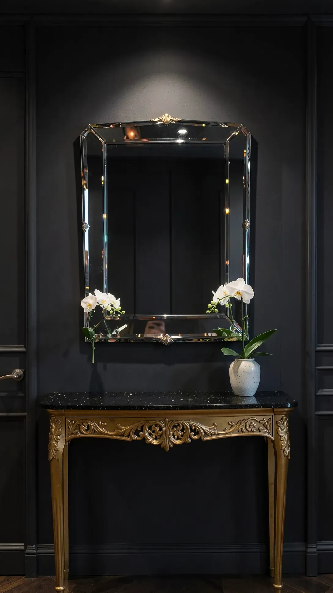 A sparkling beveled mirror on a dark charcoal wall with a gold console table.