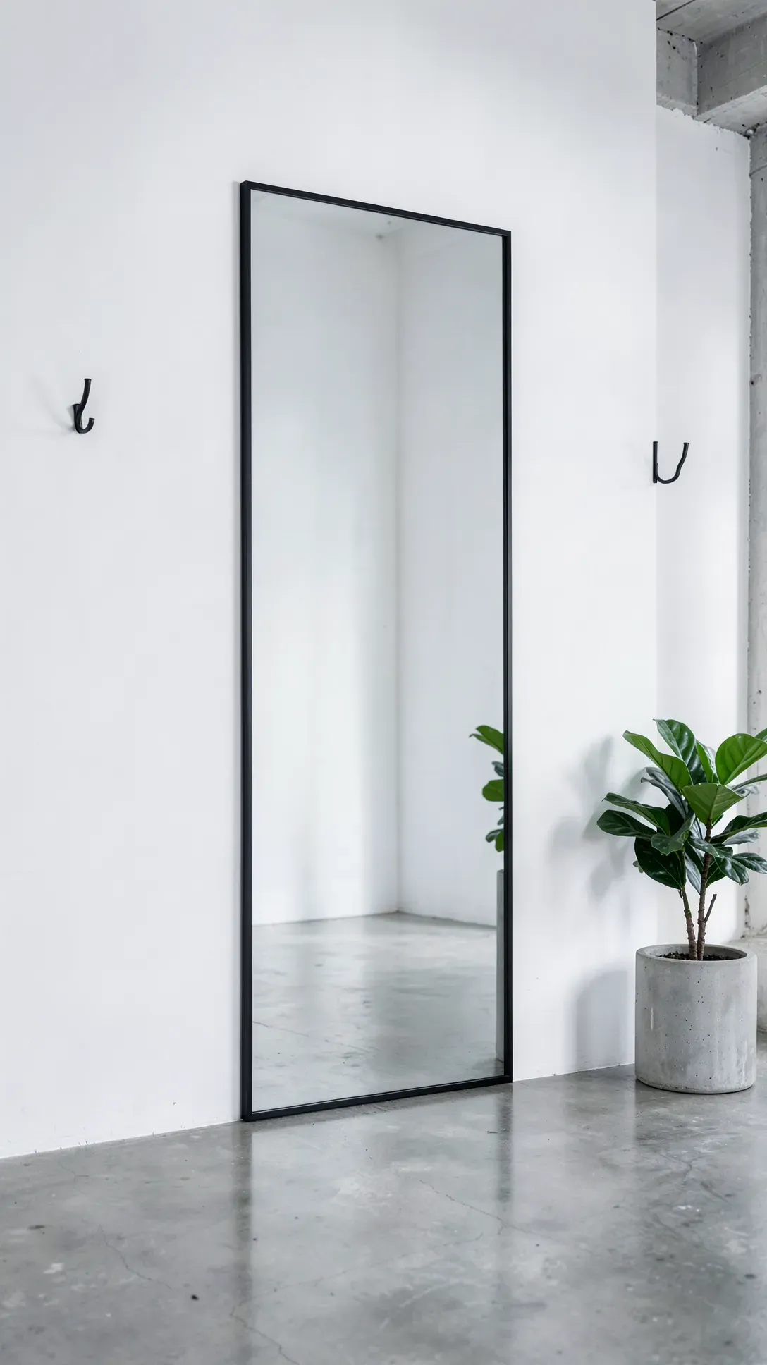 A modern vertical mirror with a thin black frame on a white wall above a polished concrete floor.