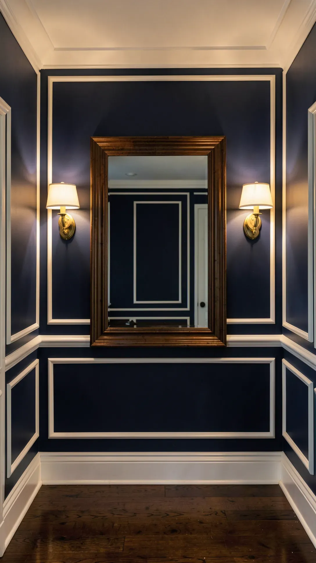 A centered dark wood mirror flanked by two brass wall sconces on a navy blue entryway wall.