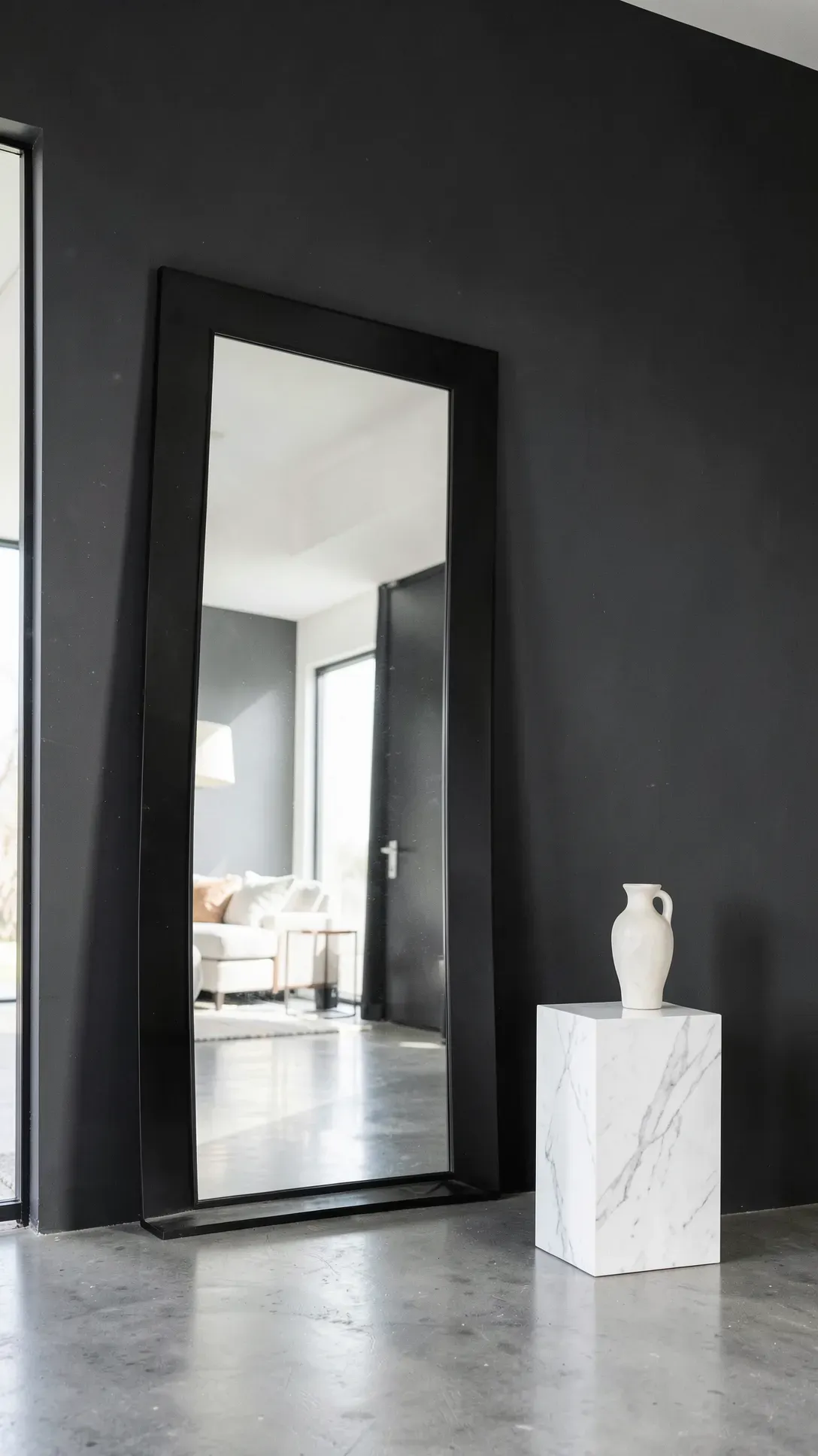 A large rectangular mirror leaning against a dark gray wall, reflecting a bright room.