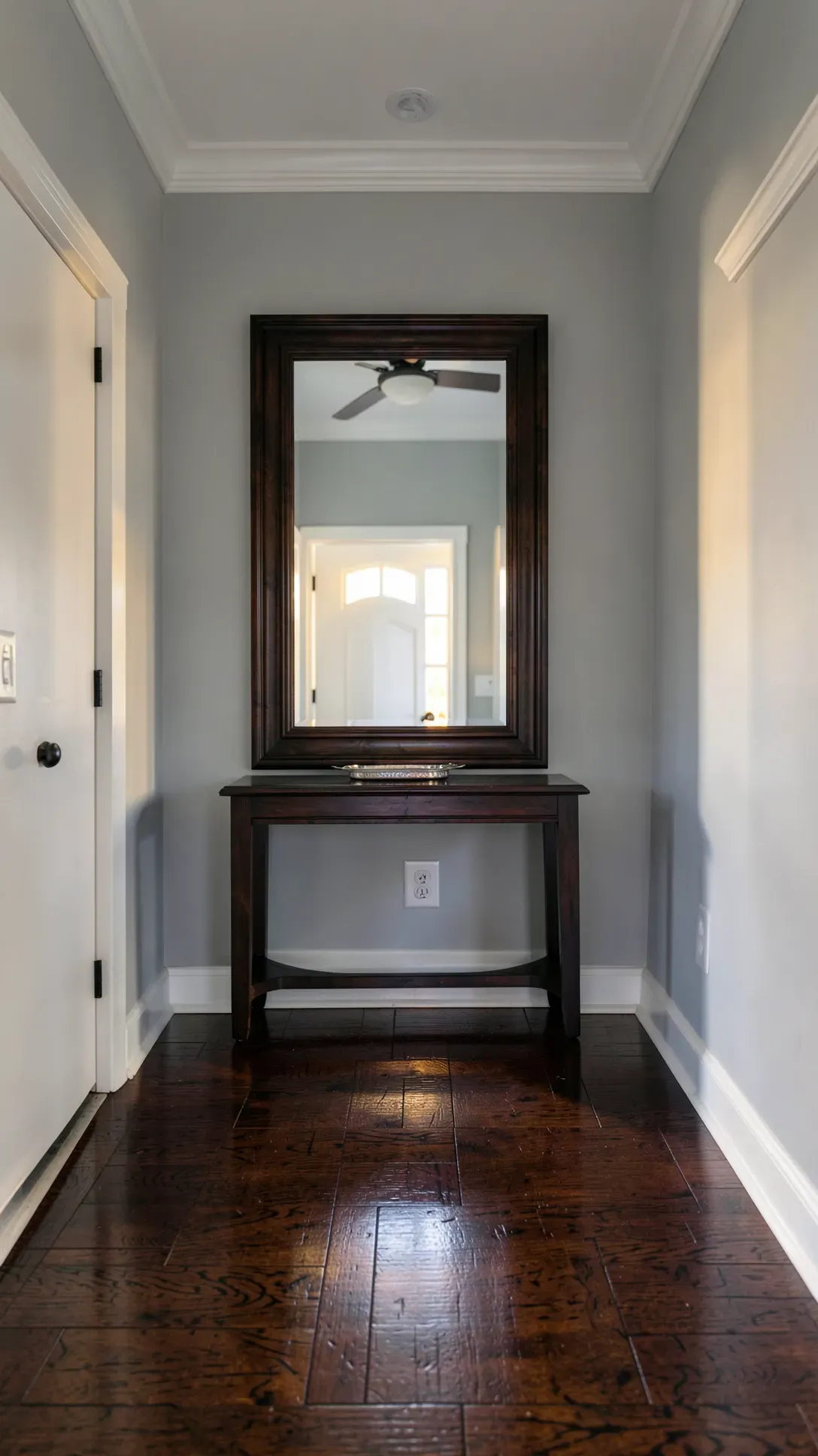 A dark wood framed mirror matches the polished walnut floors in a sophisticated entryway.
