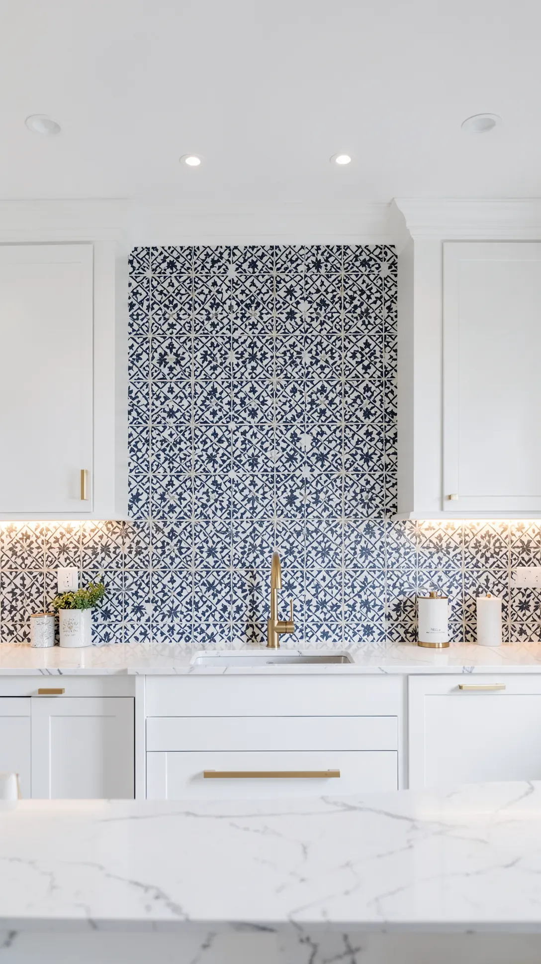 A detailed navy and white stenciled Moroccan tile mural on a kitchen backsplash with marble counters.