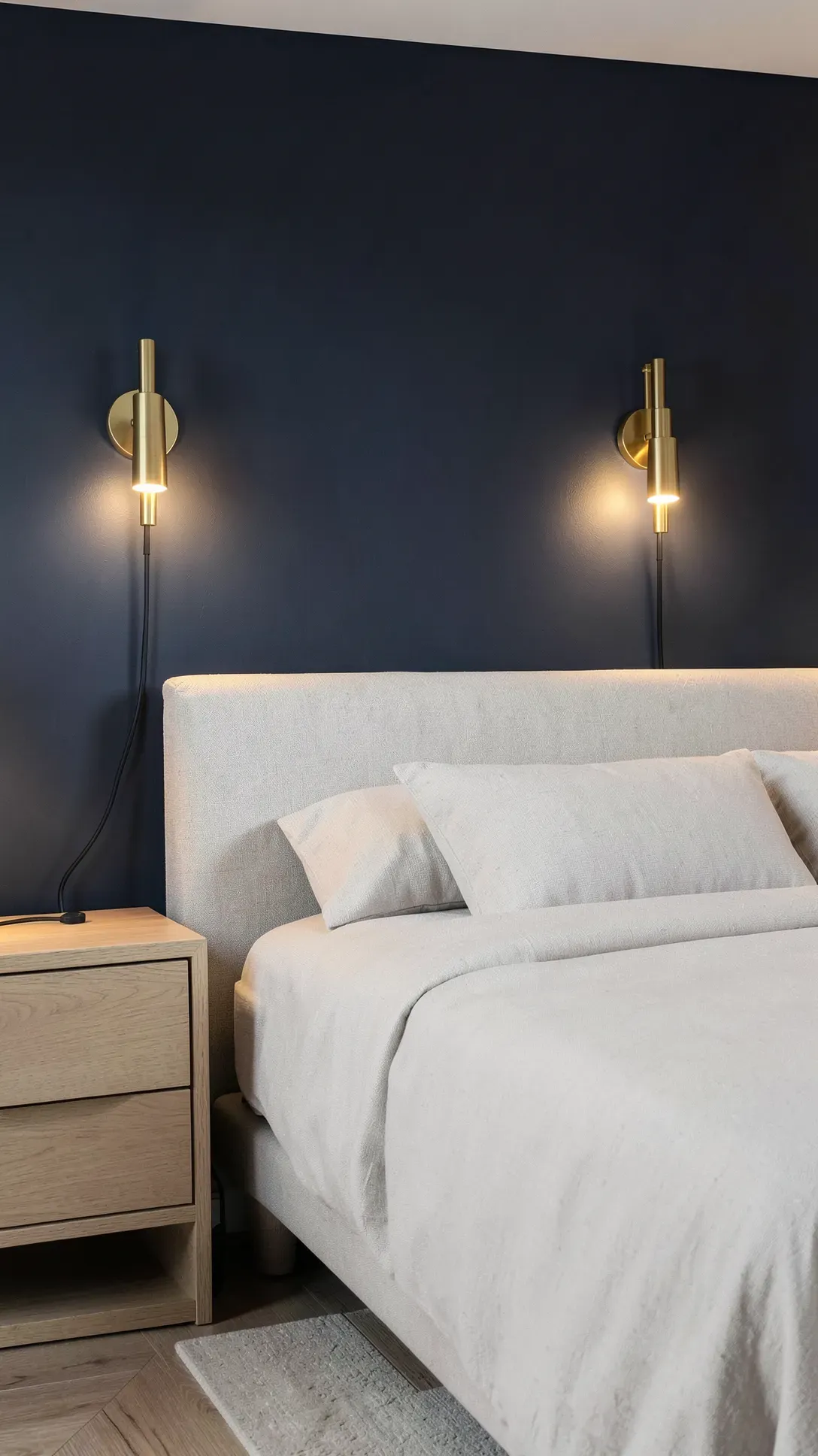 Two brass swing-arm reading lamps mounted on a navy blue wall on both sides of a bed.