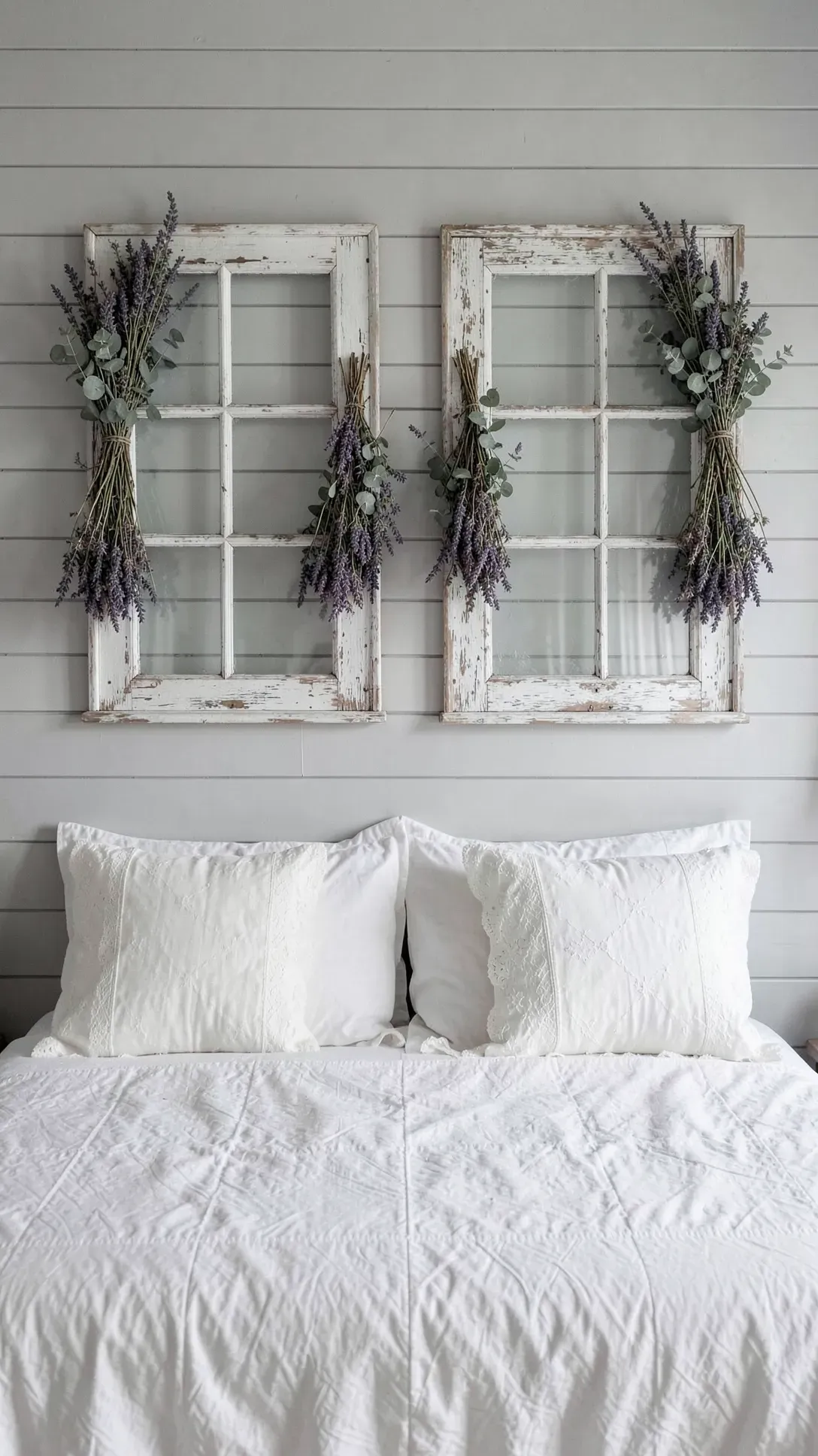 Two vintage wooden window frames with dried flowers hanging on a wall above a bed.