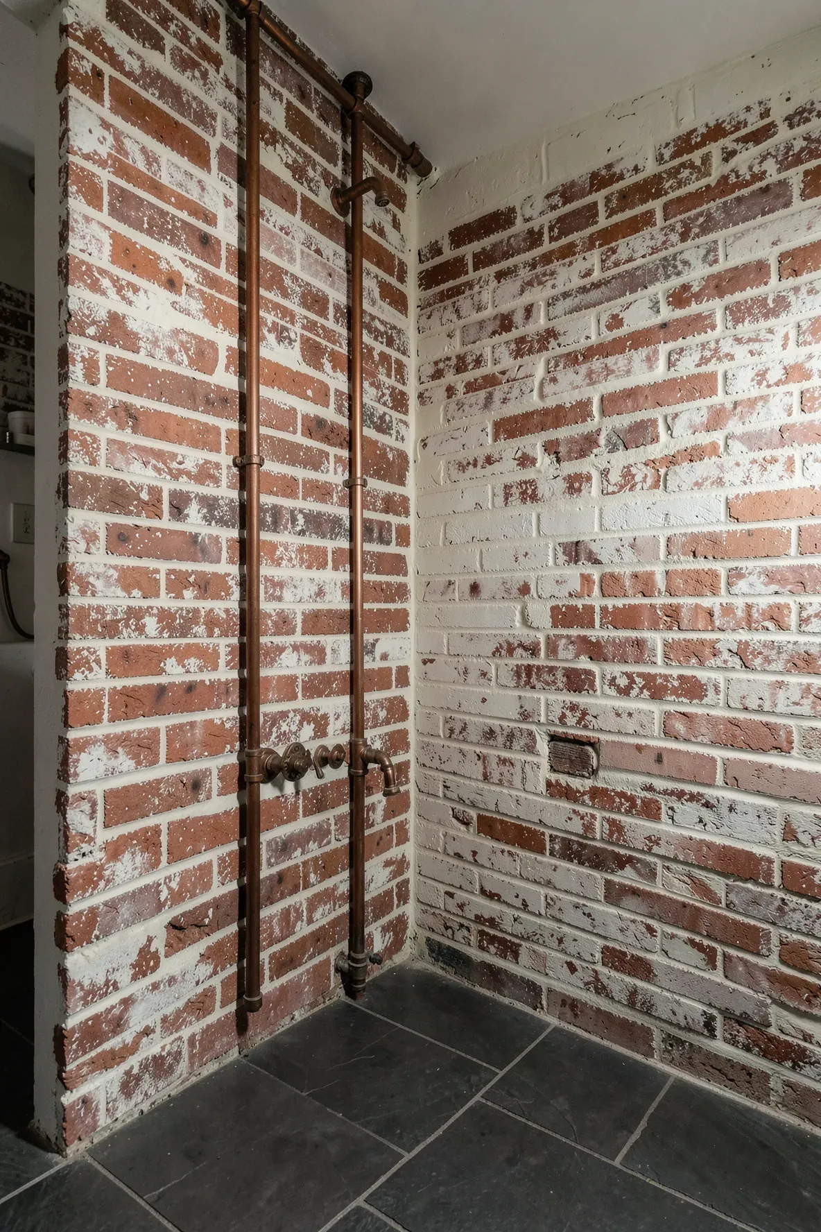 An exposed brick wall with a white lime wash in a rustic boho farmhouse bathroom.