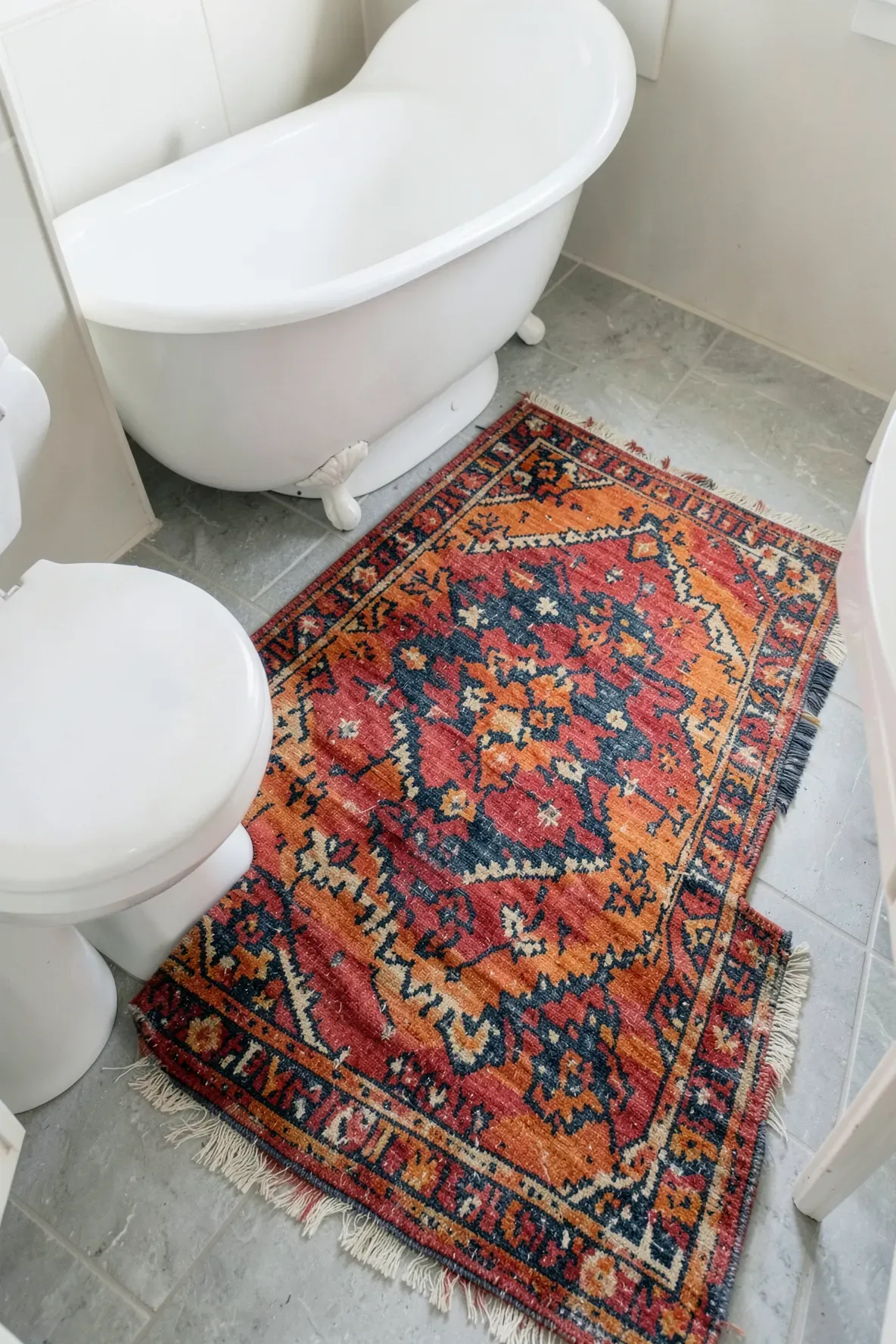 A colorful vintage Turkish kilim rug with geometric patterns serving as a bath mat in a boho bathroom.