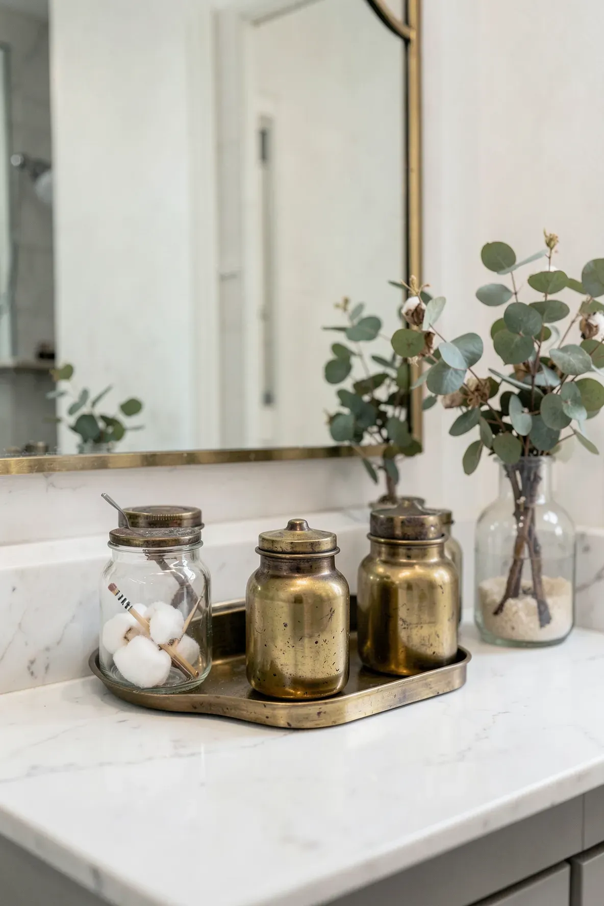 Antique brass apothecary jars containing cotton balls on a marble bathroom vanity.