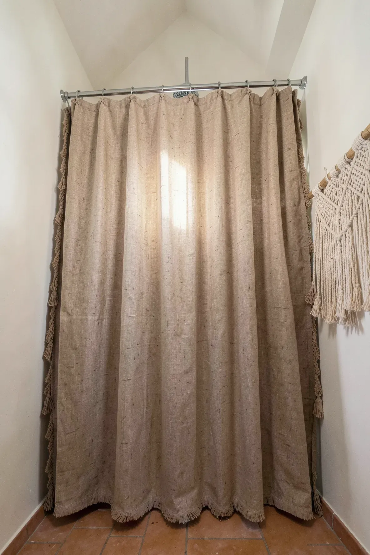 A tall oatmeal-colored linen shower curtain with tassels hanging from the ceiling in a boho bathroom.