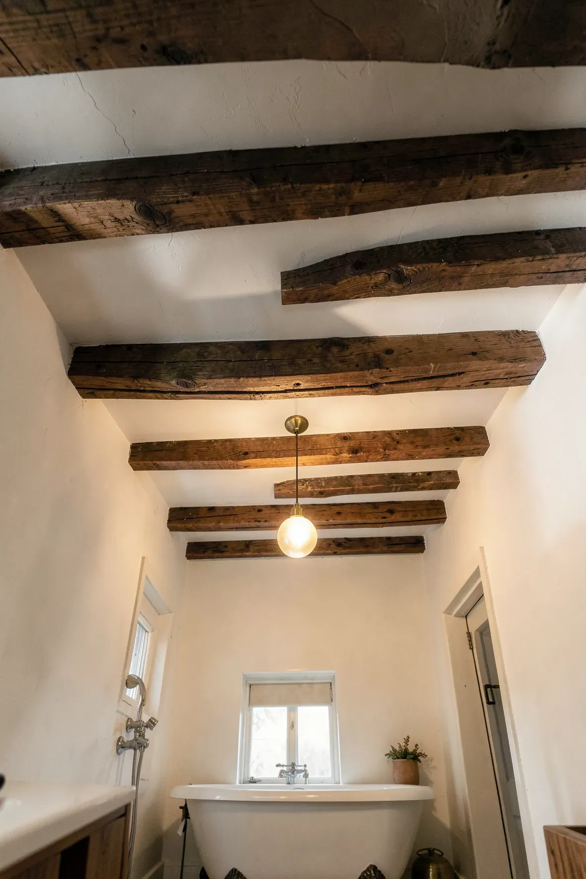 Rustic dark wood beams across the ceiling of a white bohemian farmhouse bathroom.