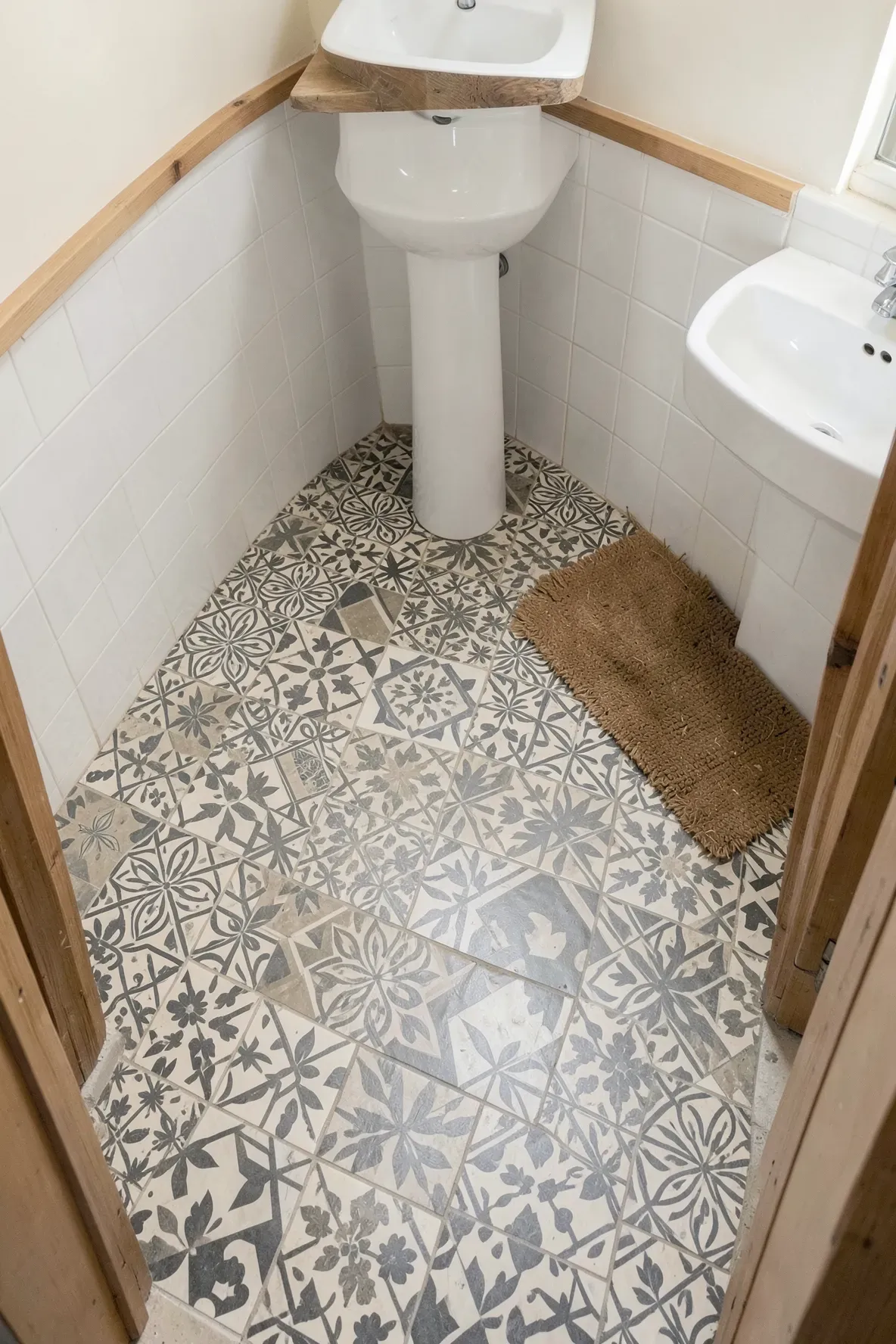A small boho bathroom floor featuring a variety of mismatched geometric tiles in neutral grey and cream.