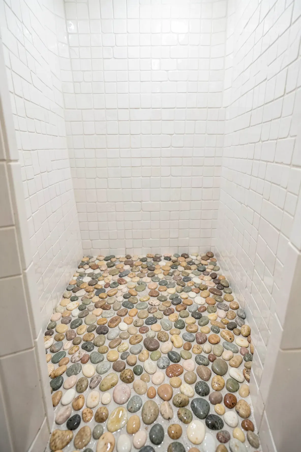 A walk-in shower with a natural river stone pebble floor and white tiled walls.