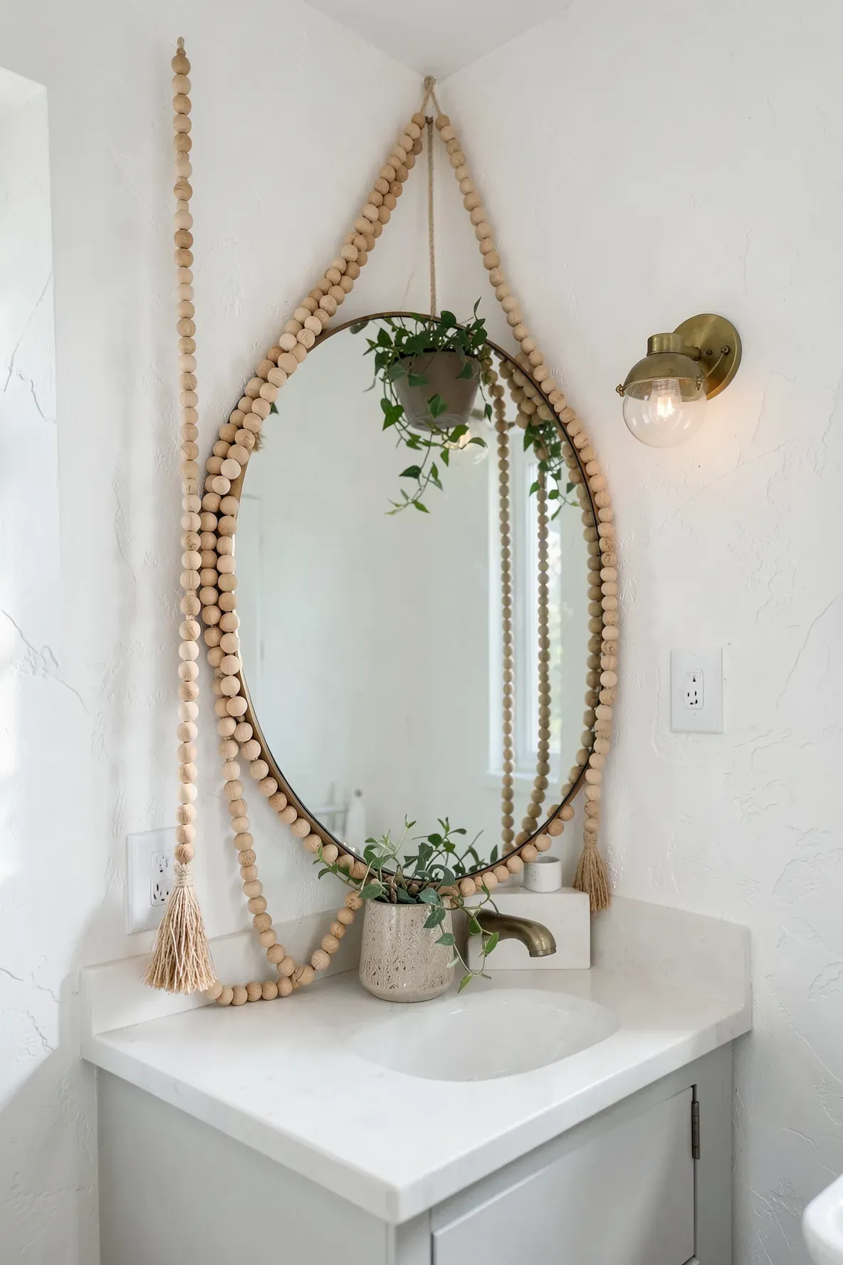 A round bathroom mirror with a natural wood bead garland draped over its top corner.