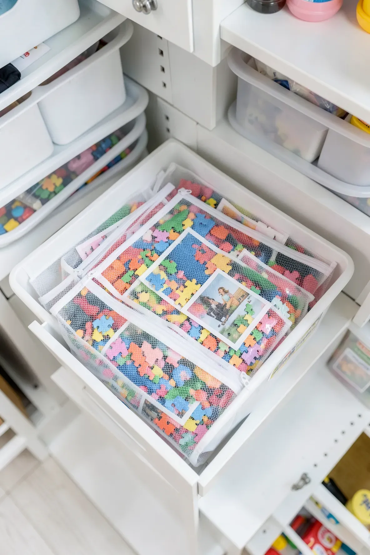Neatly organized mesh bags filled with puzzle pieces inside a white storage bin on a shelf.
