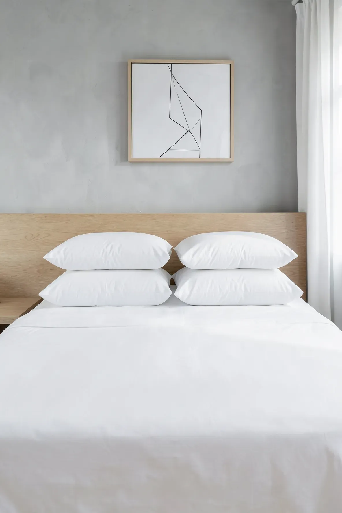 A minimalist bed with white pillows stacked flat behind two large upright square shams against a wooden headboard.