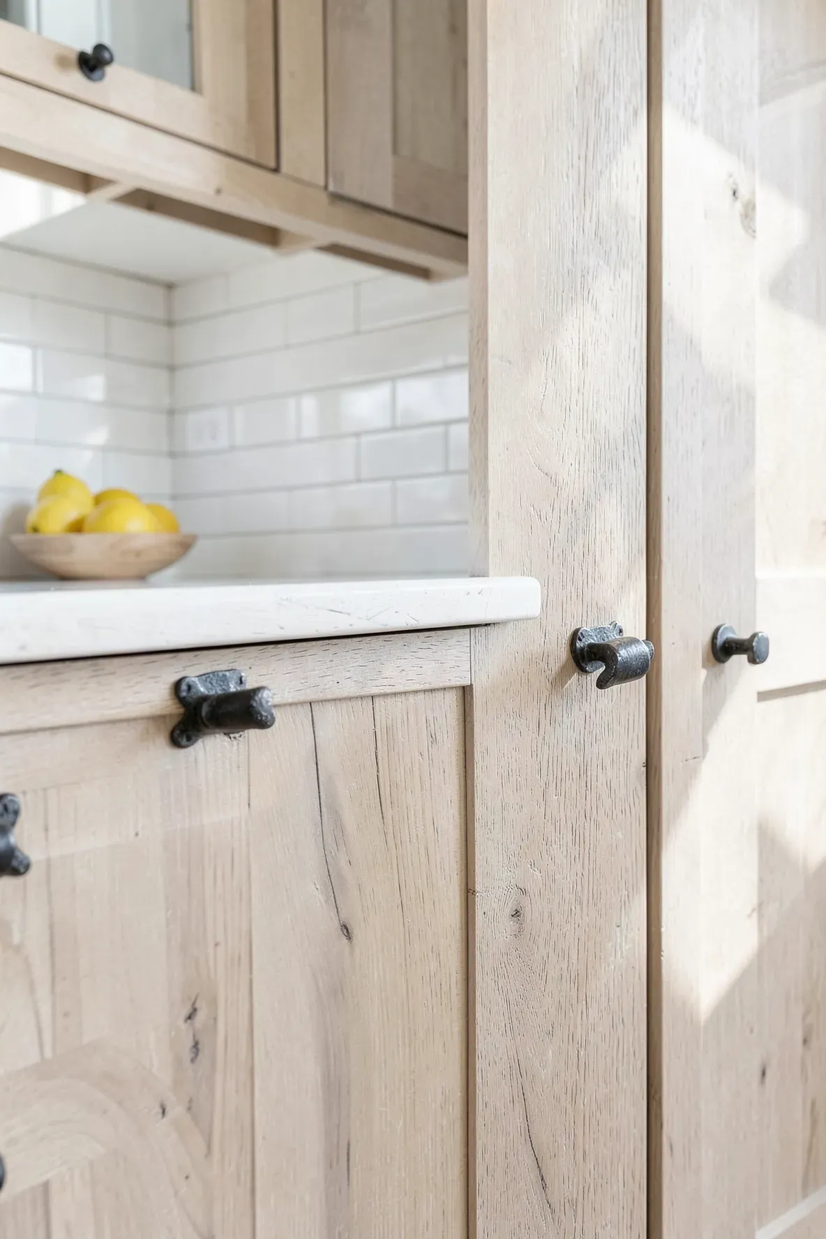 Hand-forged iron cabinet pulls with a dark patina on light wood cabinets in a coastal kitchen.