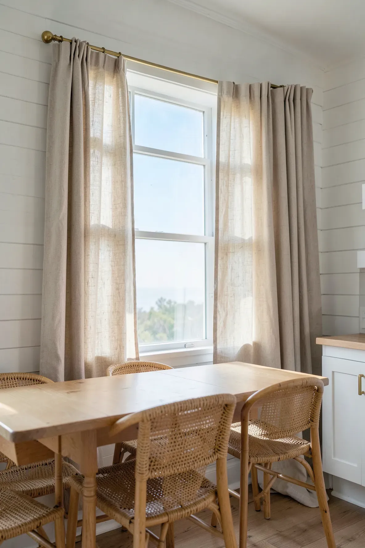 Oatmeal-colored linen cafe curtains on a kitchen window in a breezy coastal-style home.