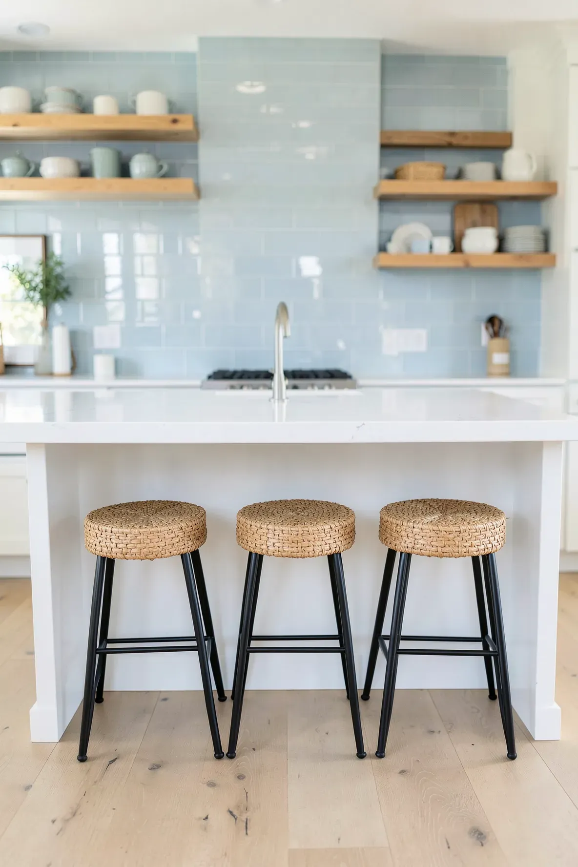 Three woven seagrass bar stools with black metal legs at a white kitchen island.